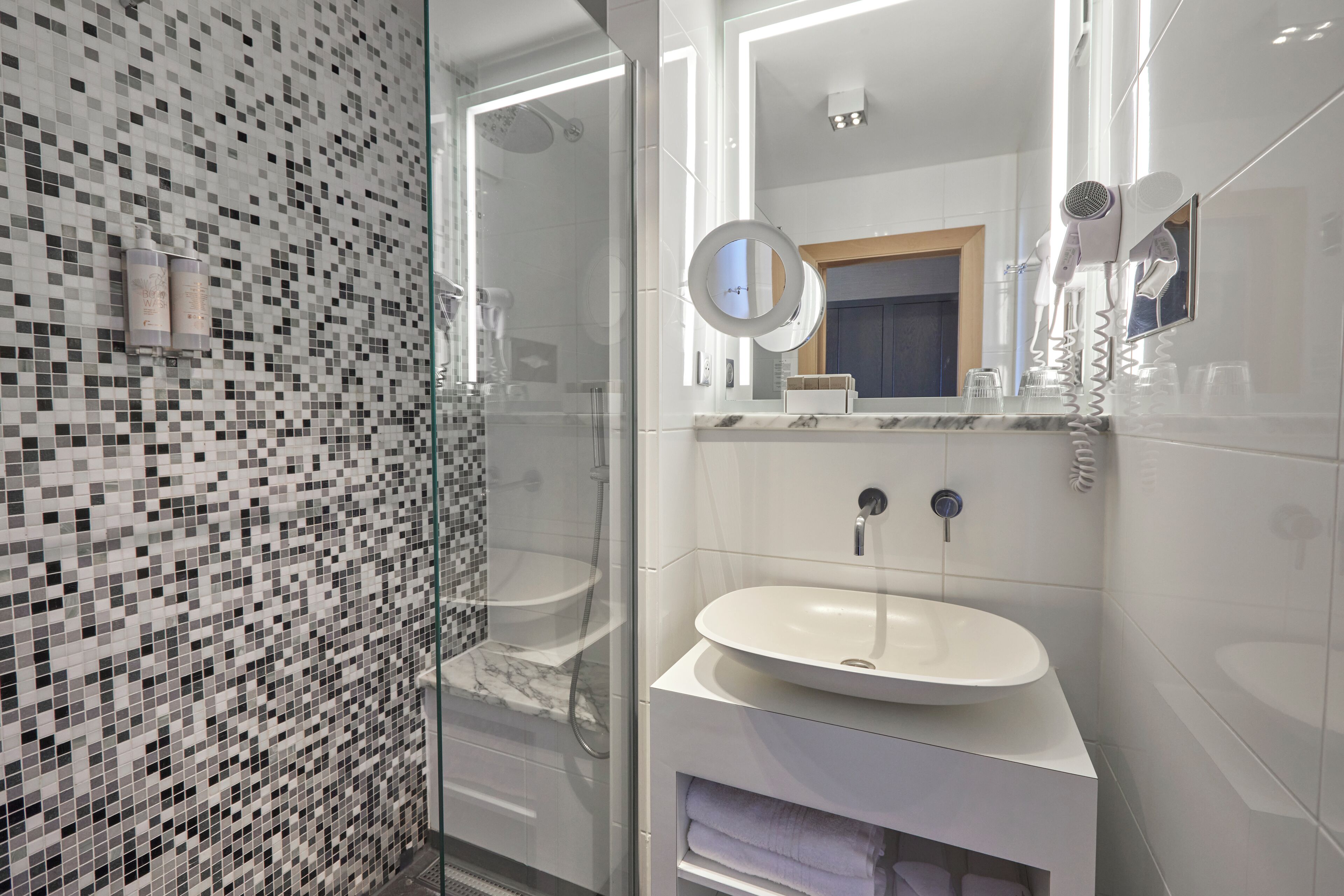 Une salle de bain moderne avec une douche à l’italienne en verre, un lavabo blanc et un miroir doté d’un anneau lumineux.