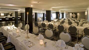A banquet hall with multiple tables set for dining, each with white tablecloths, silverware, and candles.