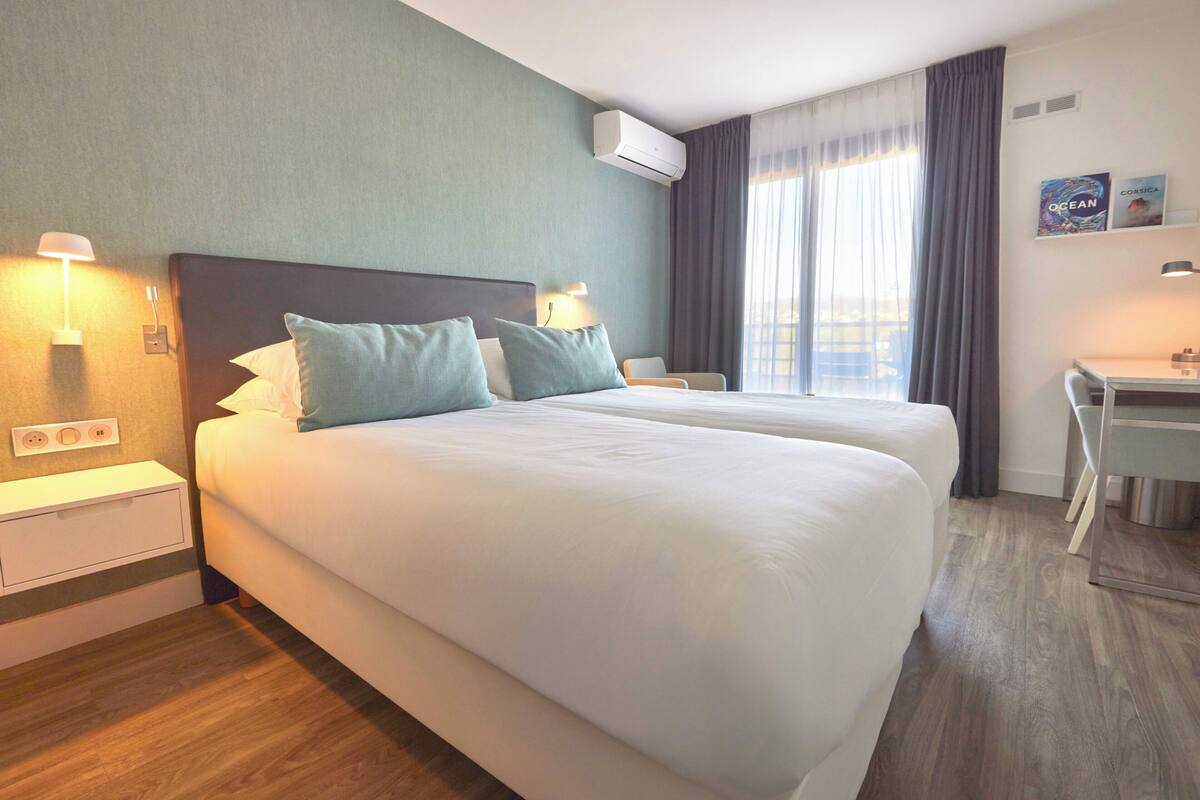 Une chambre d’hôtel avec deux lits, un bureau, une chaise, une lampe et un appareil de climatisation.