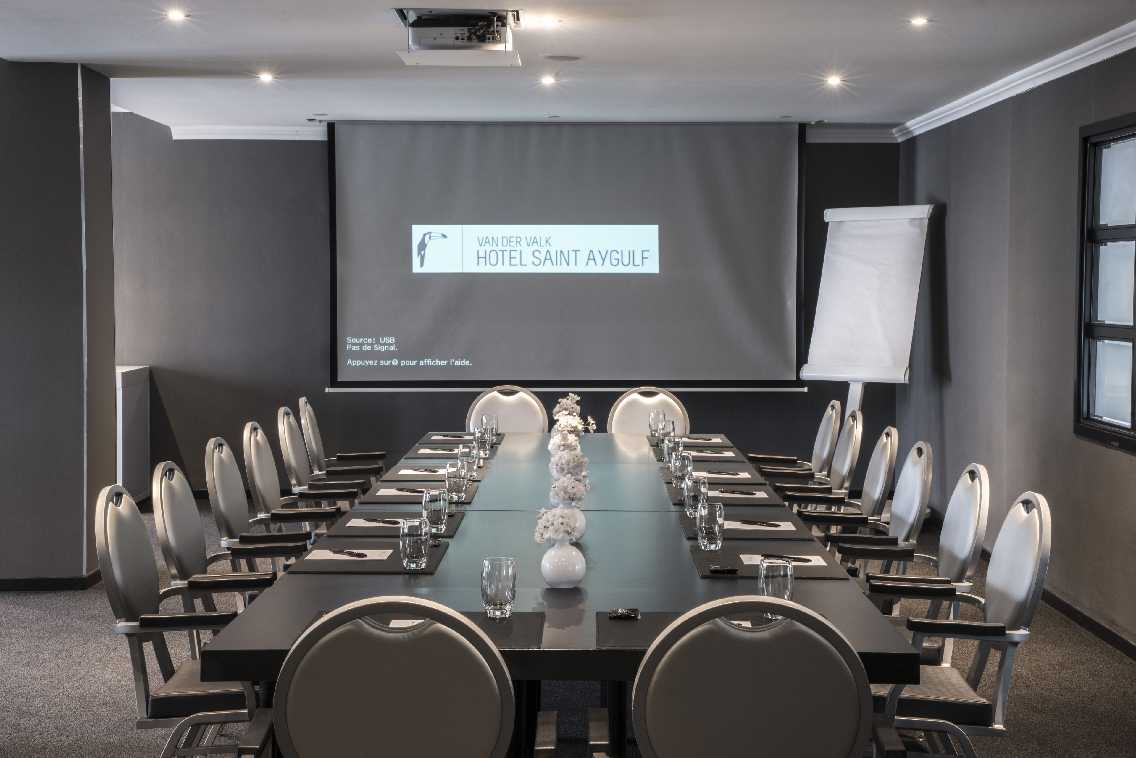 Ett konferensrum med ett långt bord, stolar och en projektionsduk som visar hotellets namn.
