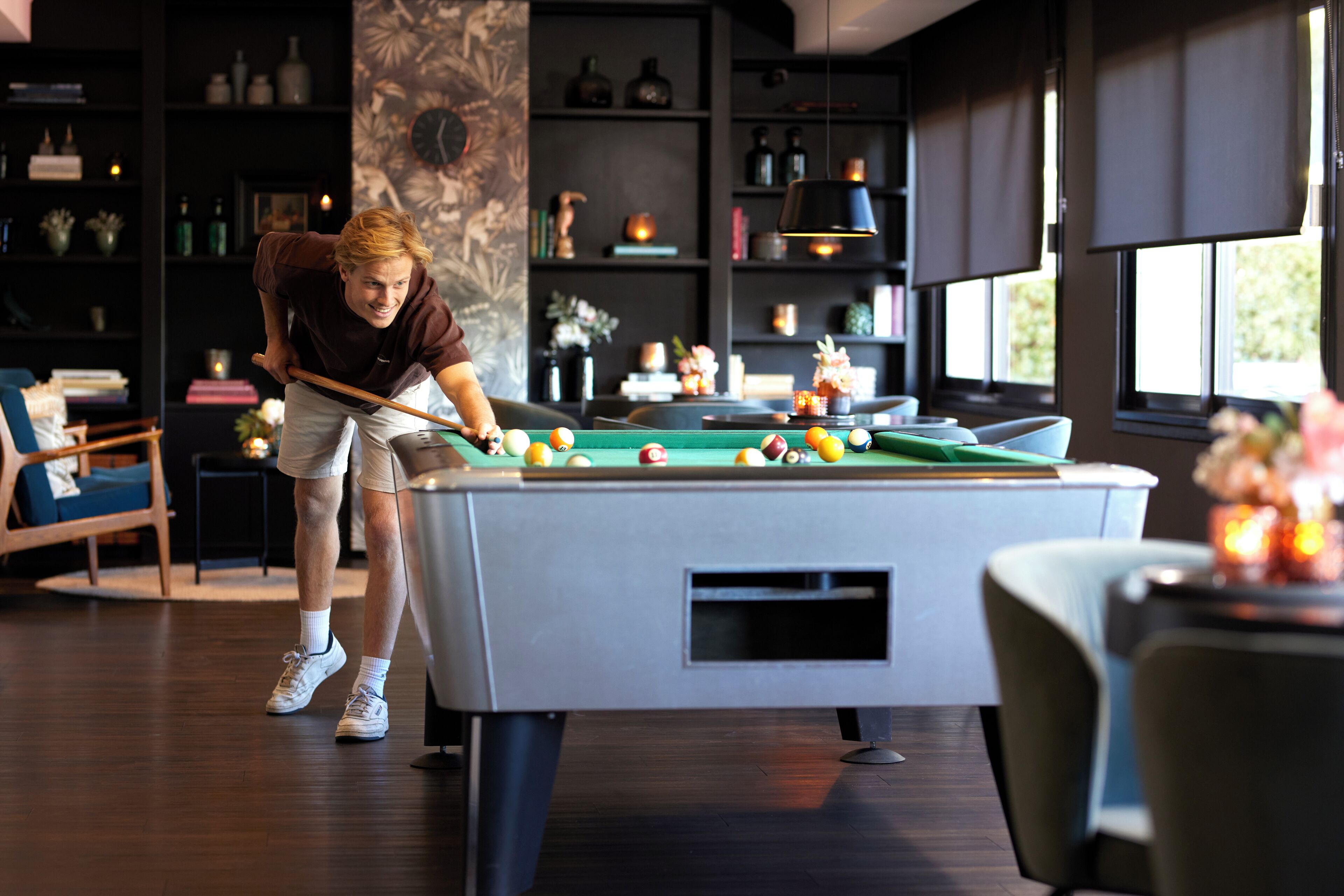 A person playing pool in a room with a pool table, bookshelves, and a modern interior design.