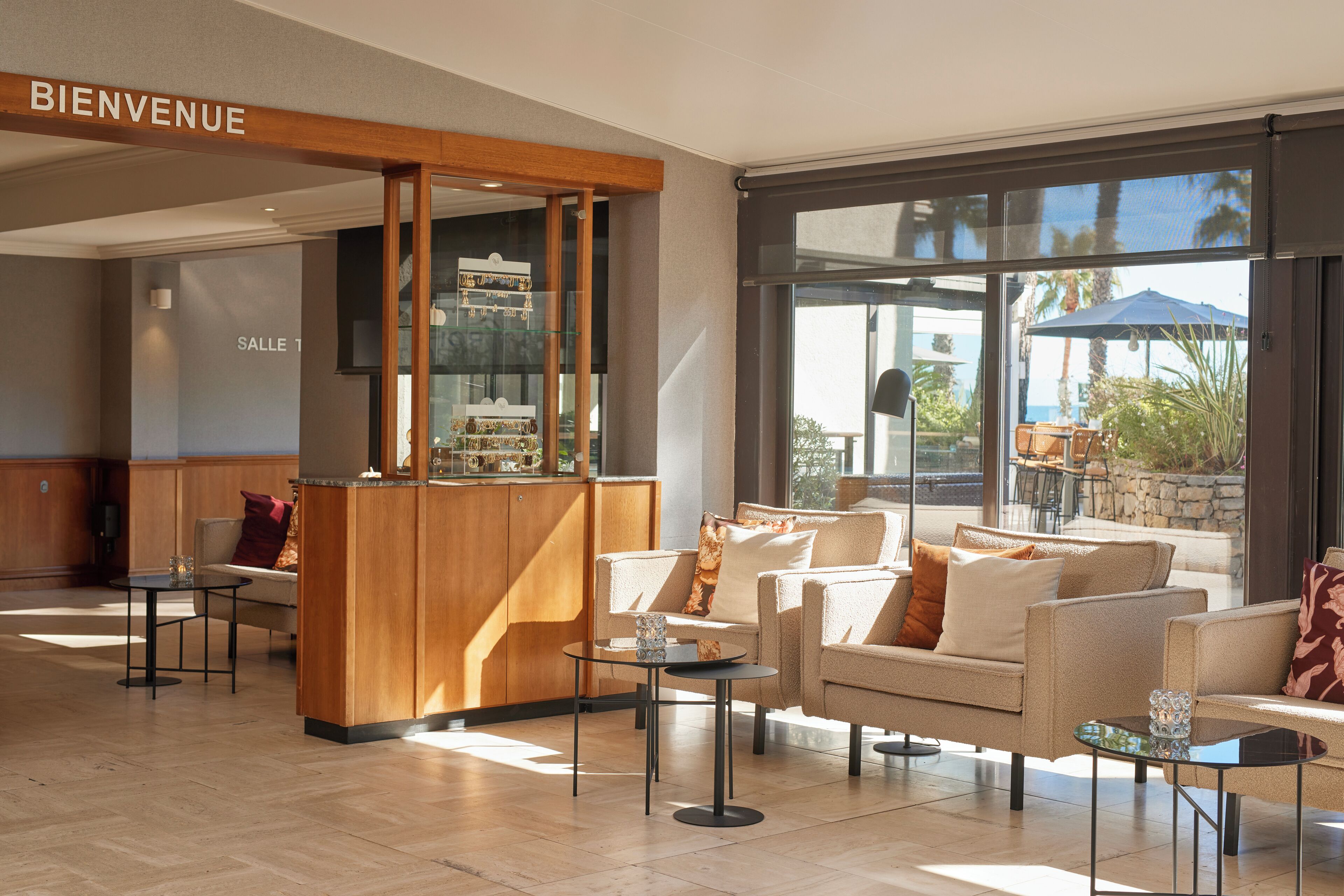A hotel lobby with a reception desk, seating area, and large windows offering views of the outdoors.