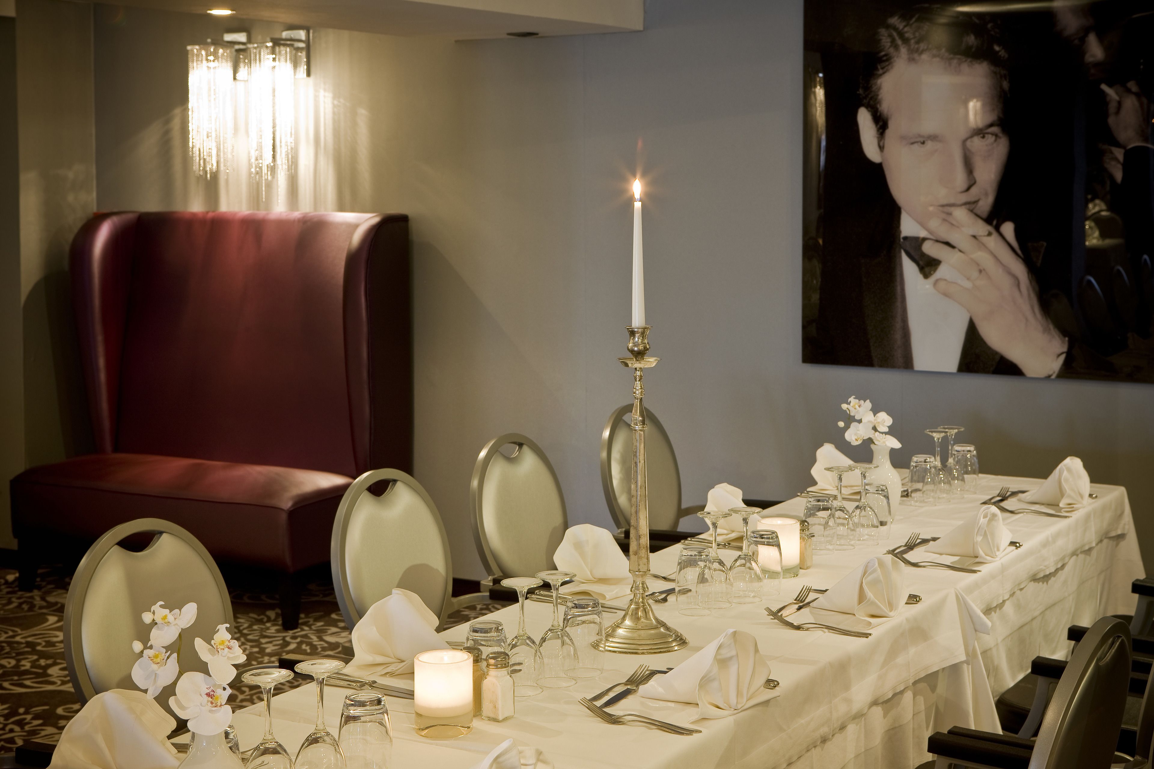 Mesa de jantar posta para uma refeição formal, com castiçal aceso, toalha de mesa branca e talheres.