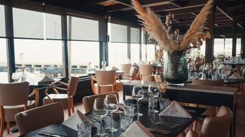Un restaurant amb taules preparades per dinar, grans finestres i una vista de la ciutat.