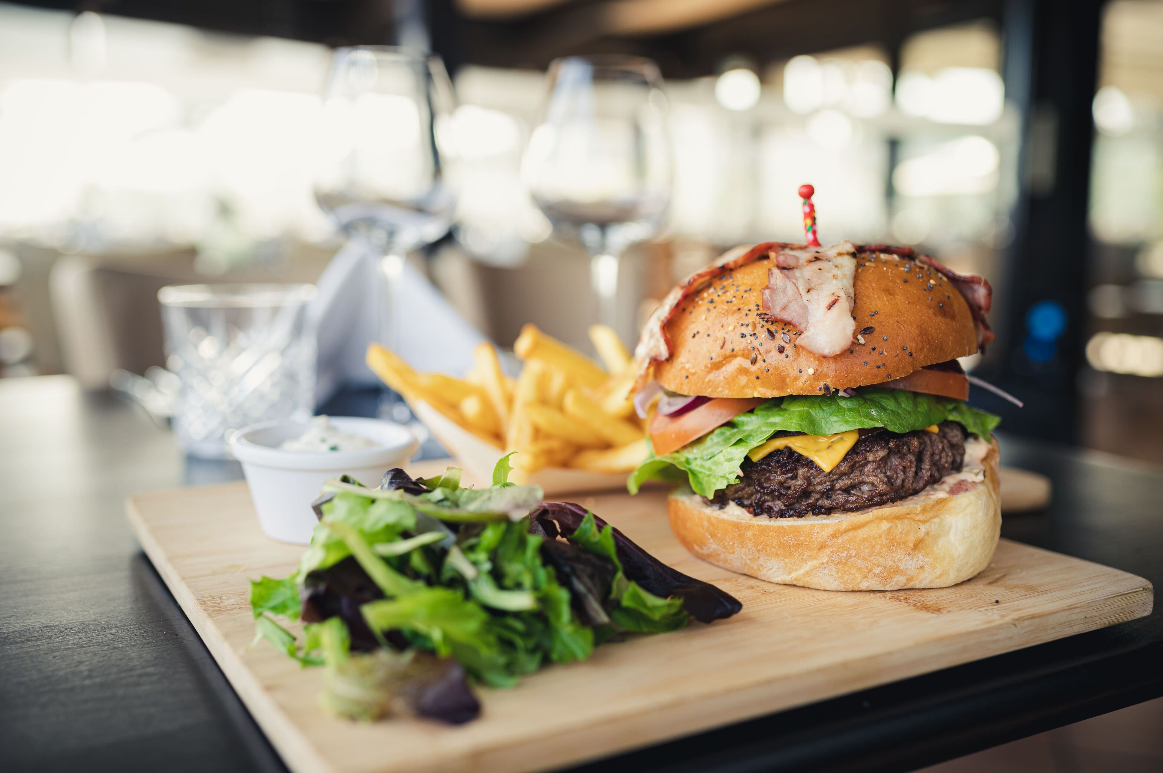 Ein Burger mit Pommes und Salat auf einer Holzplatte.