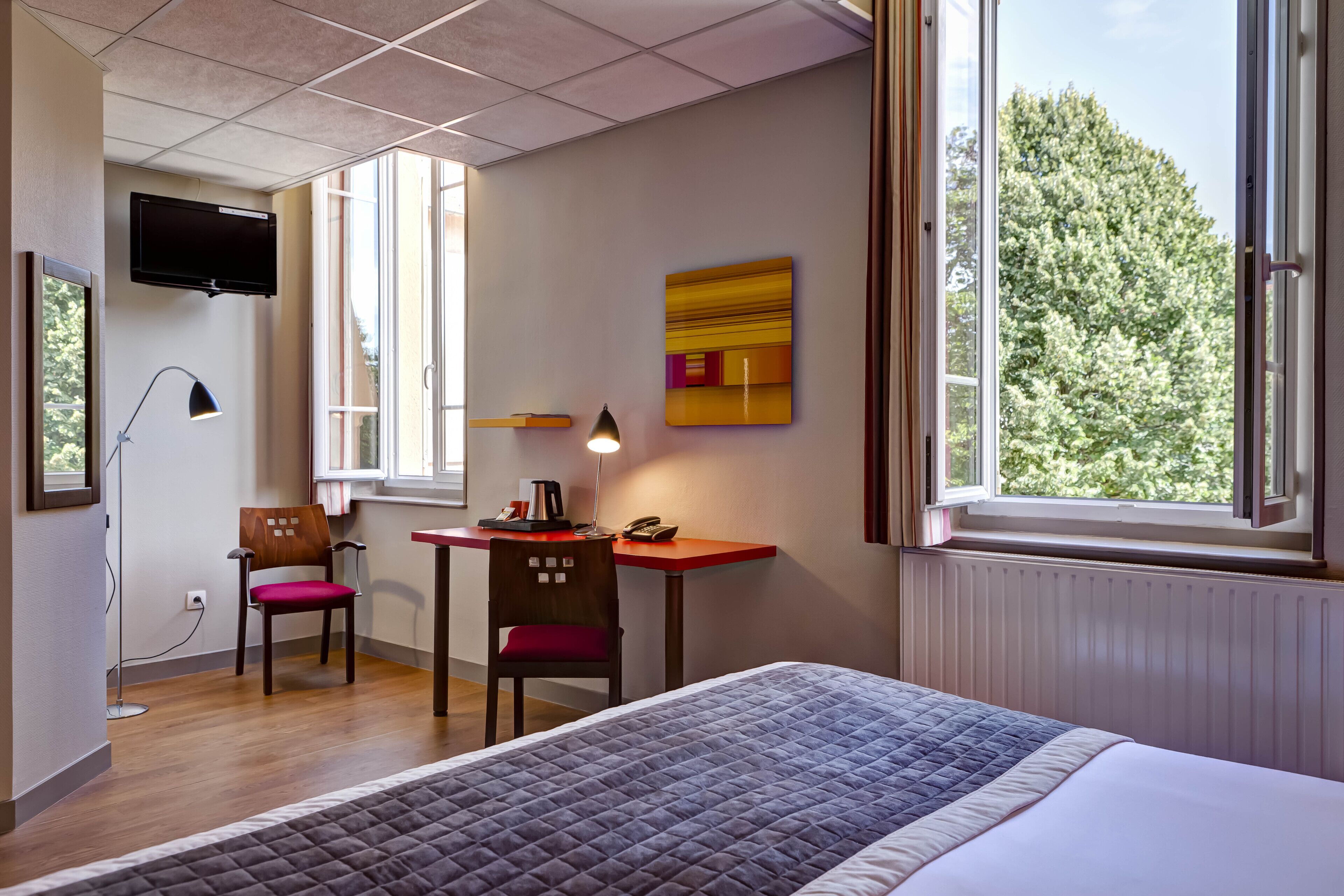 A hotel room with a bed, desk, chair, and a TV mounted on the wall.