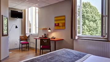 Une chambre d’hôtel équipée d’un lit, d’un bureau, d’une chaise et d’un téléviseur fixé au mur.