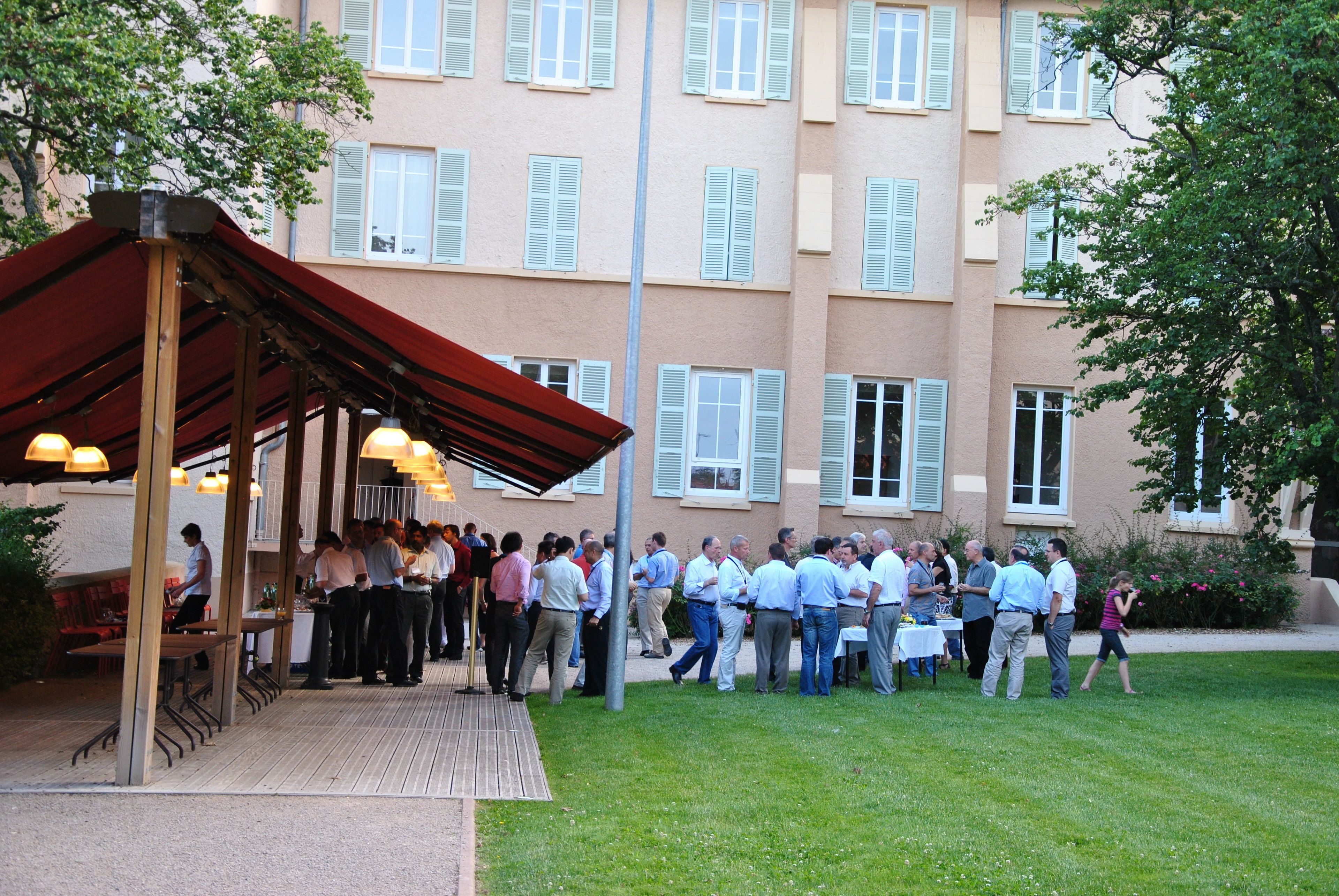 A covered outdoor area with a group of people gathered around tables, likely for an event or meeting.