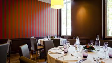 A restaurant with round tables set for dining, striped walls, and a large window.
