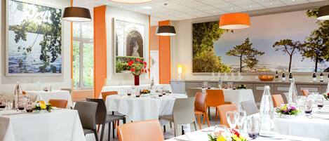 Un restaurant avec des nappes blanches, des chaises orange et des lampes orange suspendues au plafond.