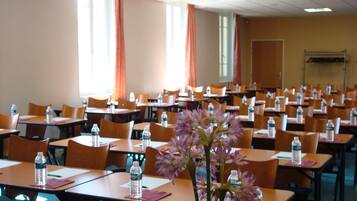 A conference room with rows of tables and chairs, water bottles on each table, and a large window with curtains.