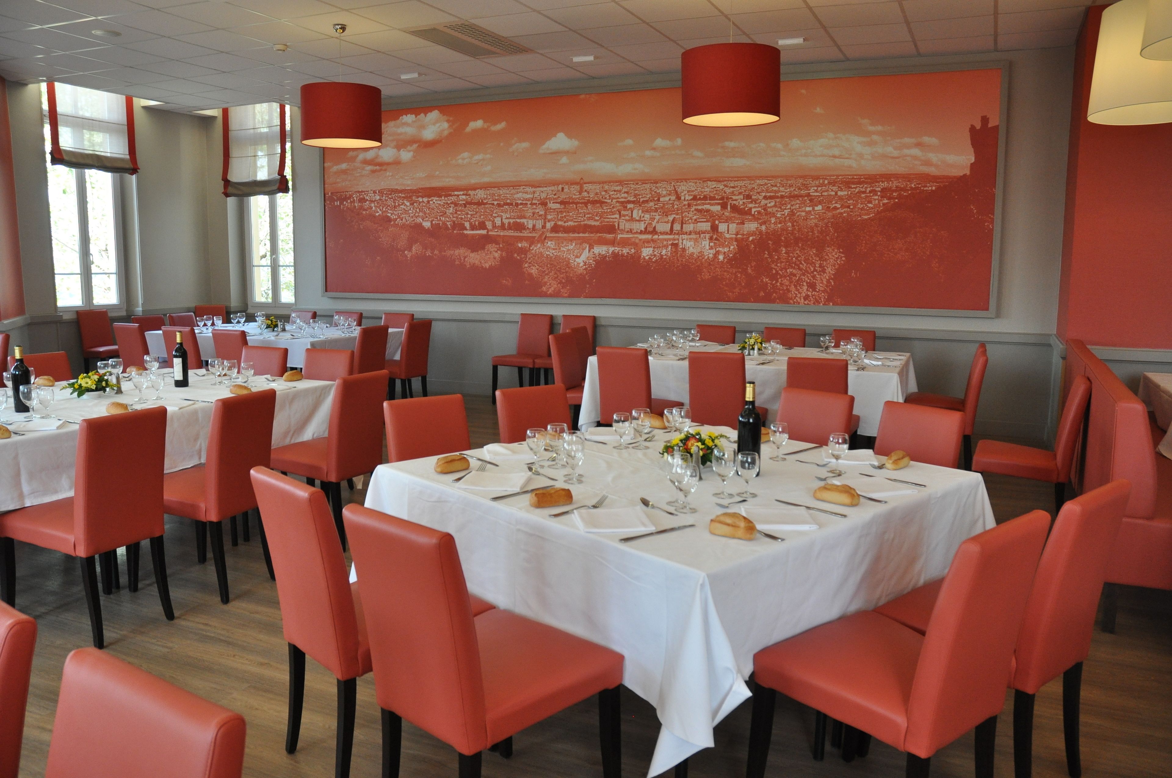 A restaurant with multiple tables set for dining, red chairs, and a large cityscape mural on the wall.