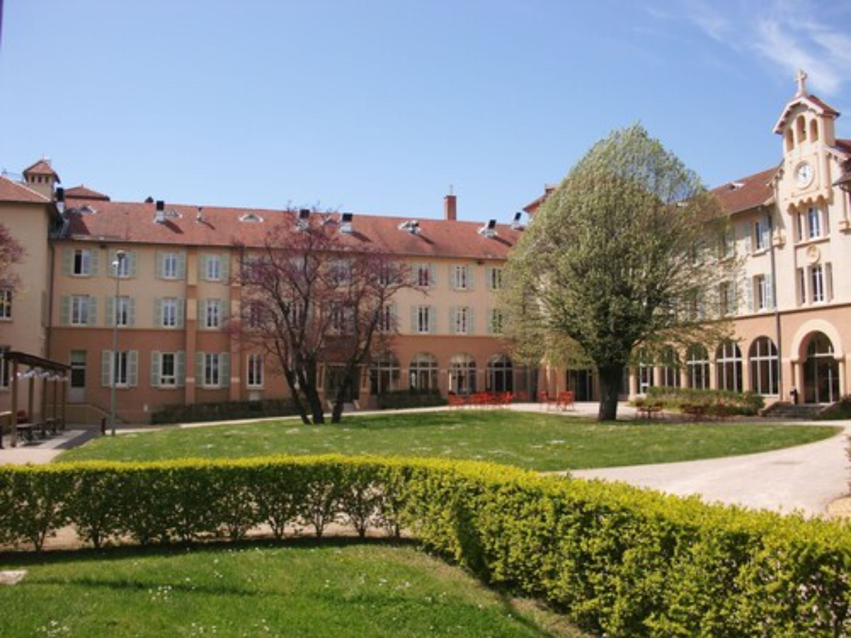 A building with a clock tower, multiple windows, and a well-maintained garden with hedges and a lawn.