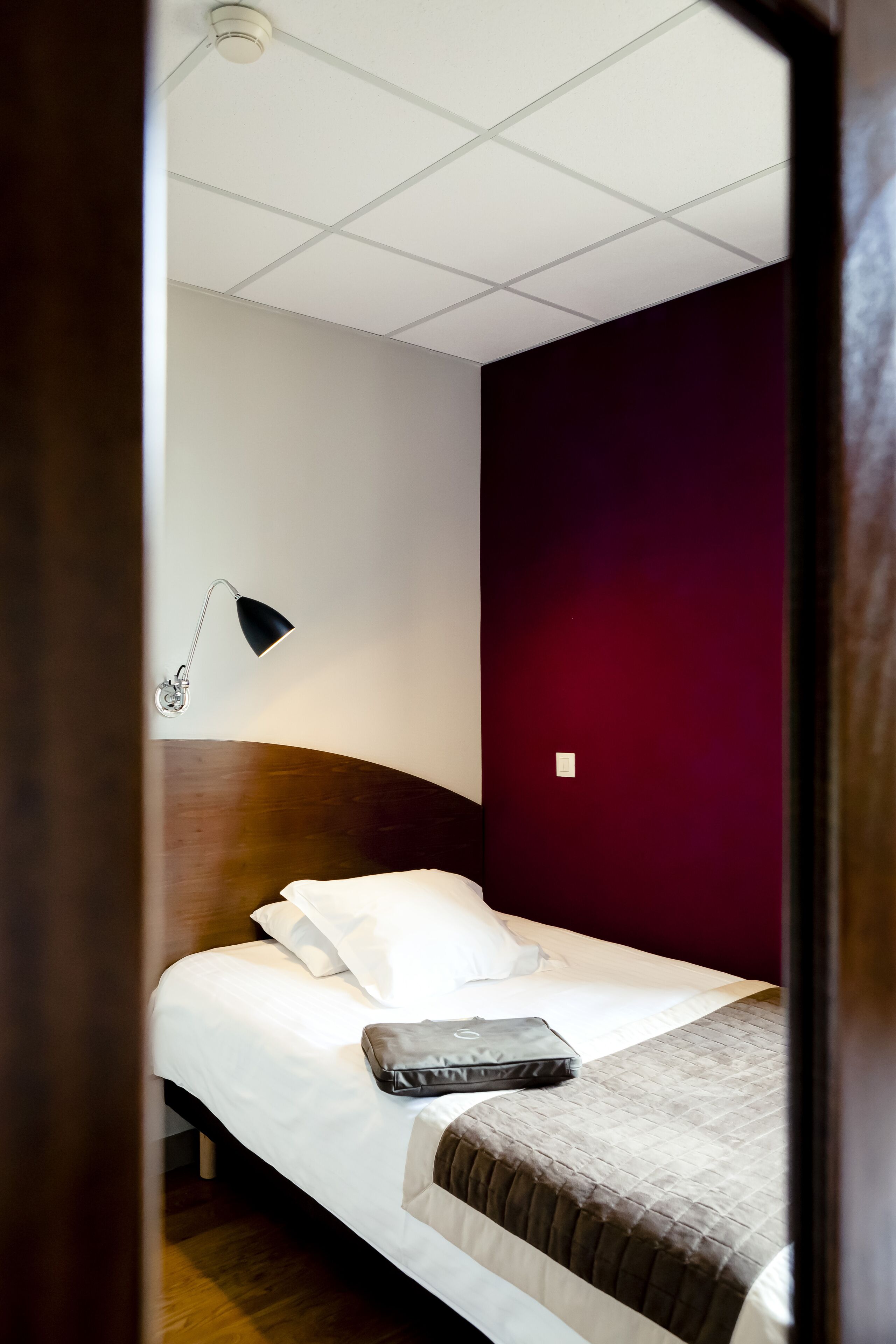 A hotel room with a bed, a desk lamp, and a dark-colored wall.