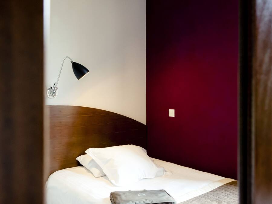 A hotel room with a bed, a desk lamp, and a dark-colored wall.