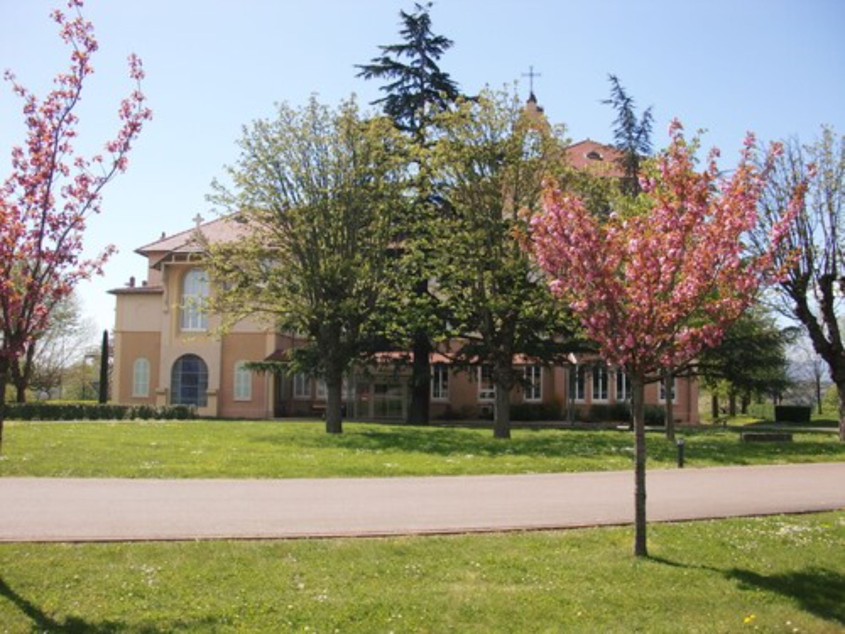A building with a cross on top, surrounded by trees and a paved walkway.