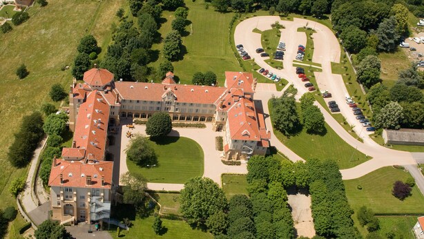 An aerial view of a large, multi-story building with a central courtyard, surrounded by lush greenery and a parking area. - Domaine Lyon Saint Joseph (Francheville)