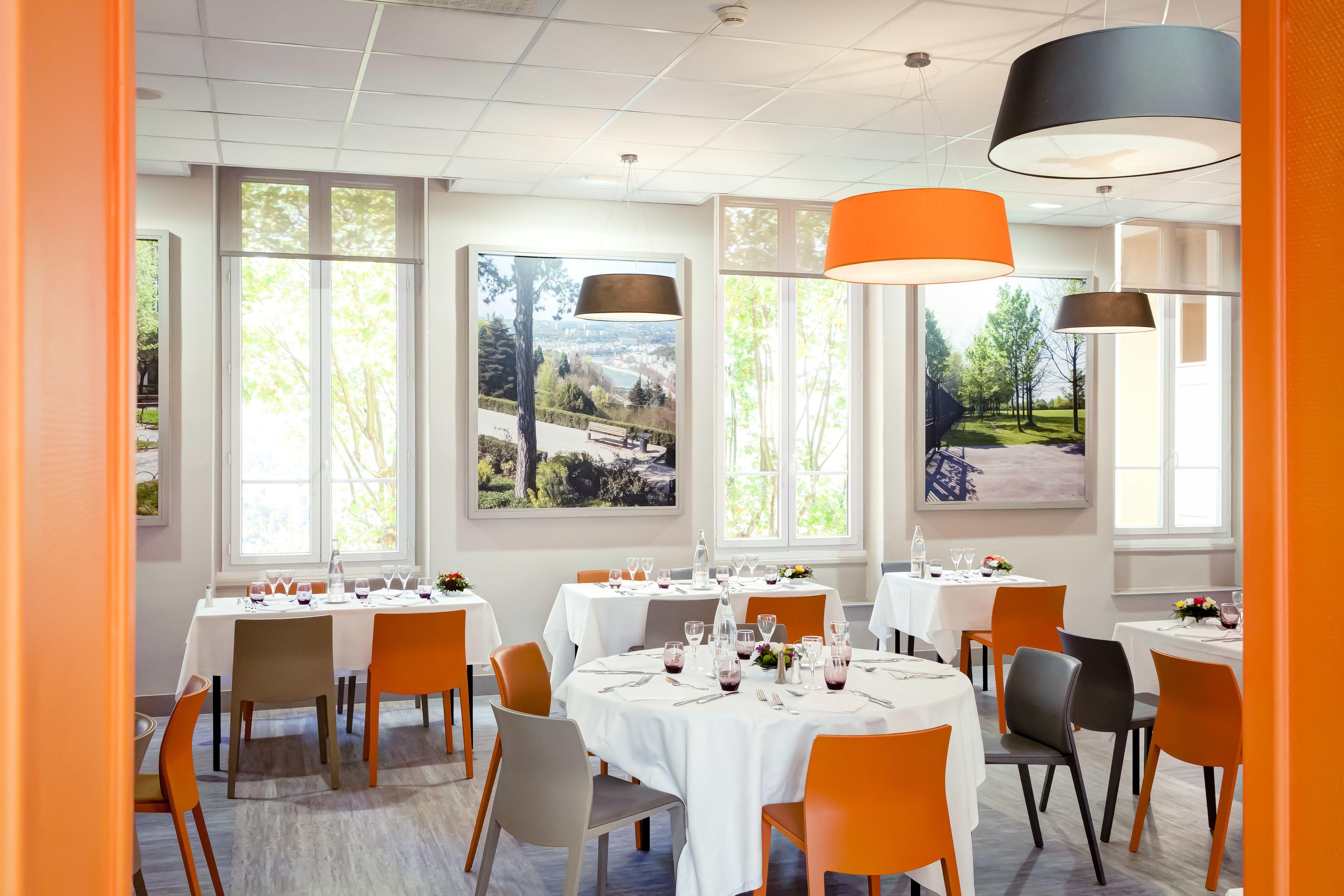 Un restaurante con mesas redondas, sillas anaranjadas y amplios ventanales con vistas al paisaje.