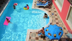 Una piscina con suelo de baldosas, sillas de descanso y sombrillas.