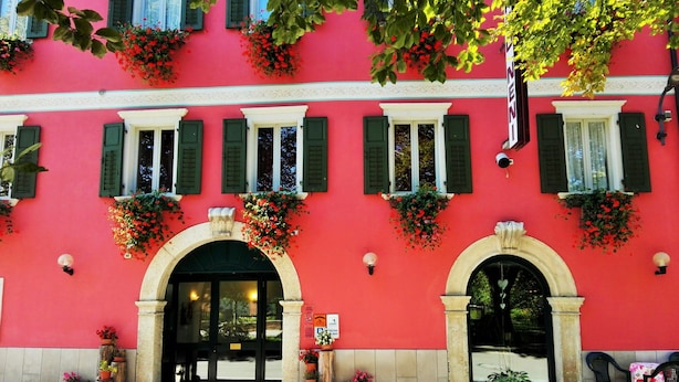 Un edificio con fachada roja, contraventanas verdes y macetas con flores.