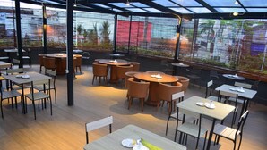 A restaurant with round tables and chairs, a wooden floor, and large windows with a view of the outside. - Yunna Hotel (Bandar Lampung)