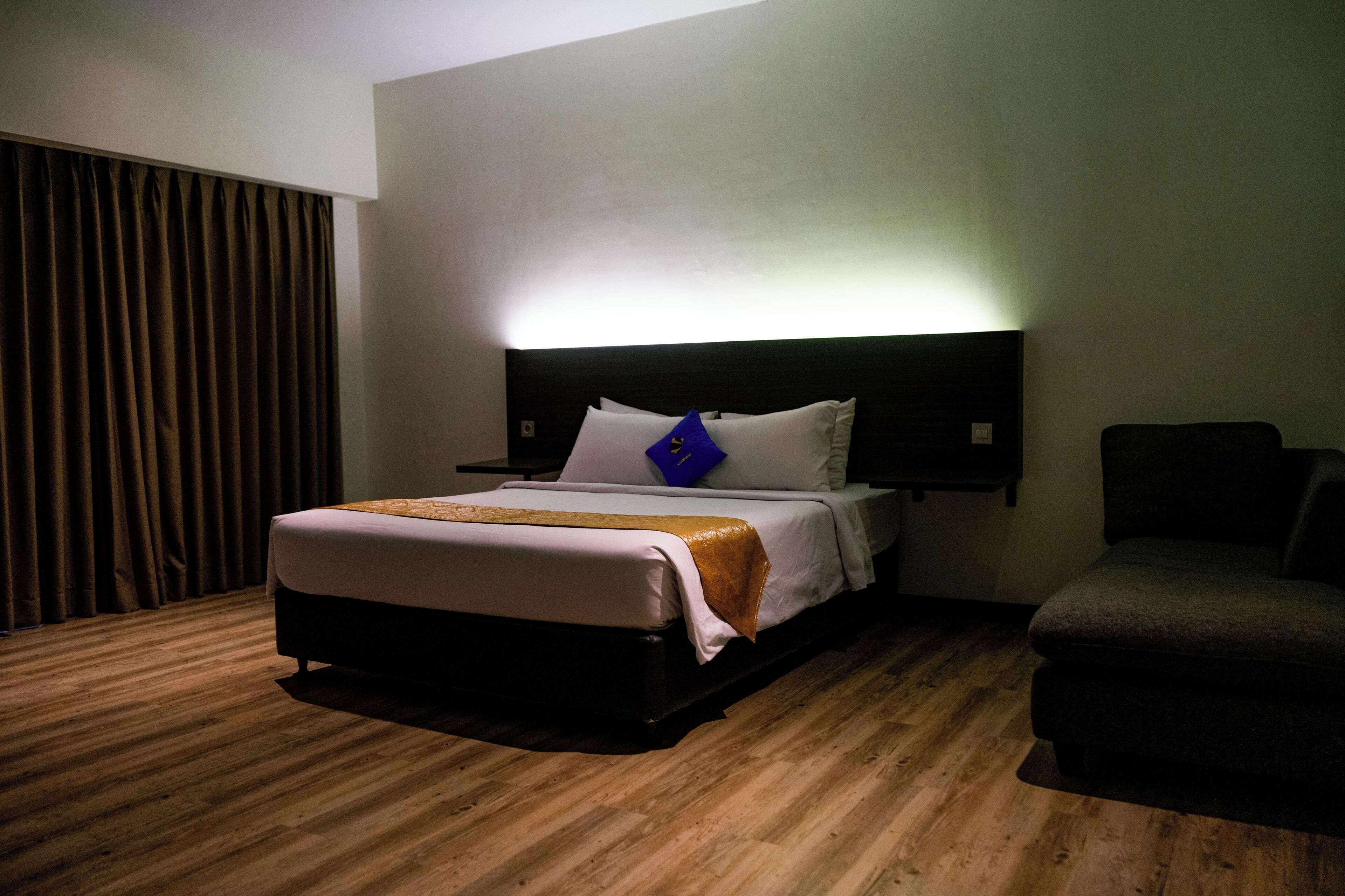 A hotel room with a bed, a headboard, a chair, and a curtain.
