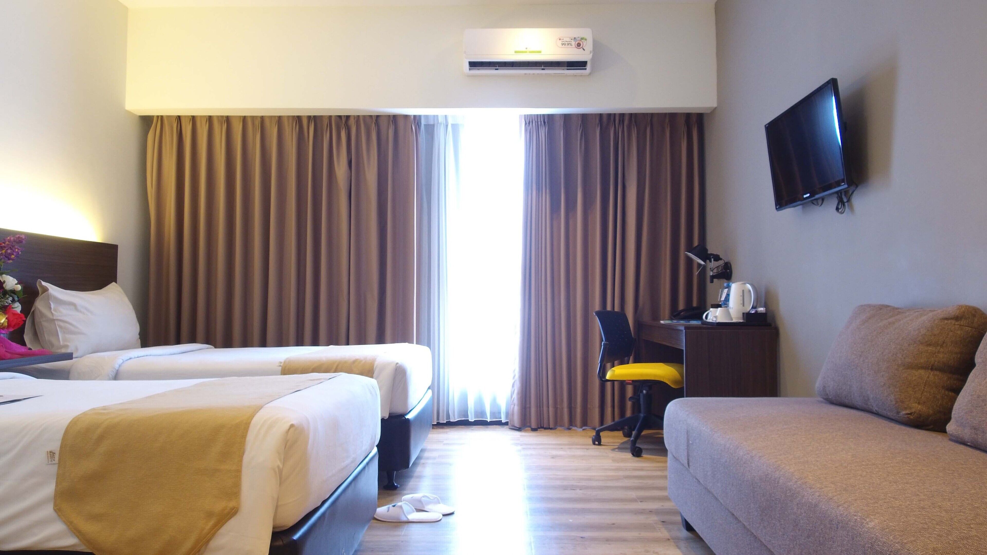 Habitación de hotel con dos camas, un escritorio con silla, televisor de pantalla plana y aire acondicionado.