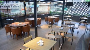 A restaurant with round and square tables, chairs, and a view of the street through large windows. - Yunna Hotel (Bandar Lampung)