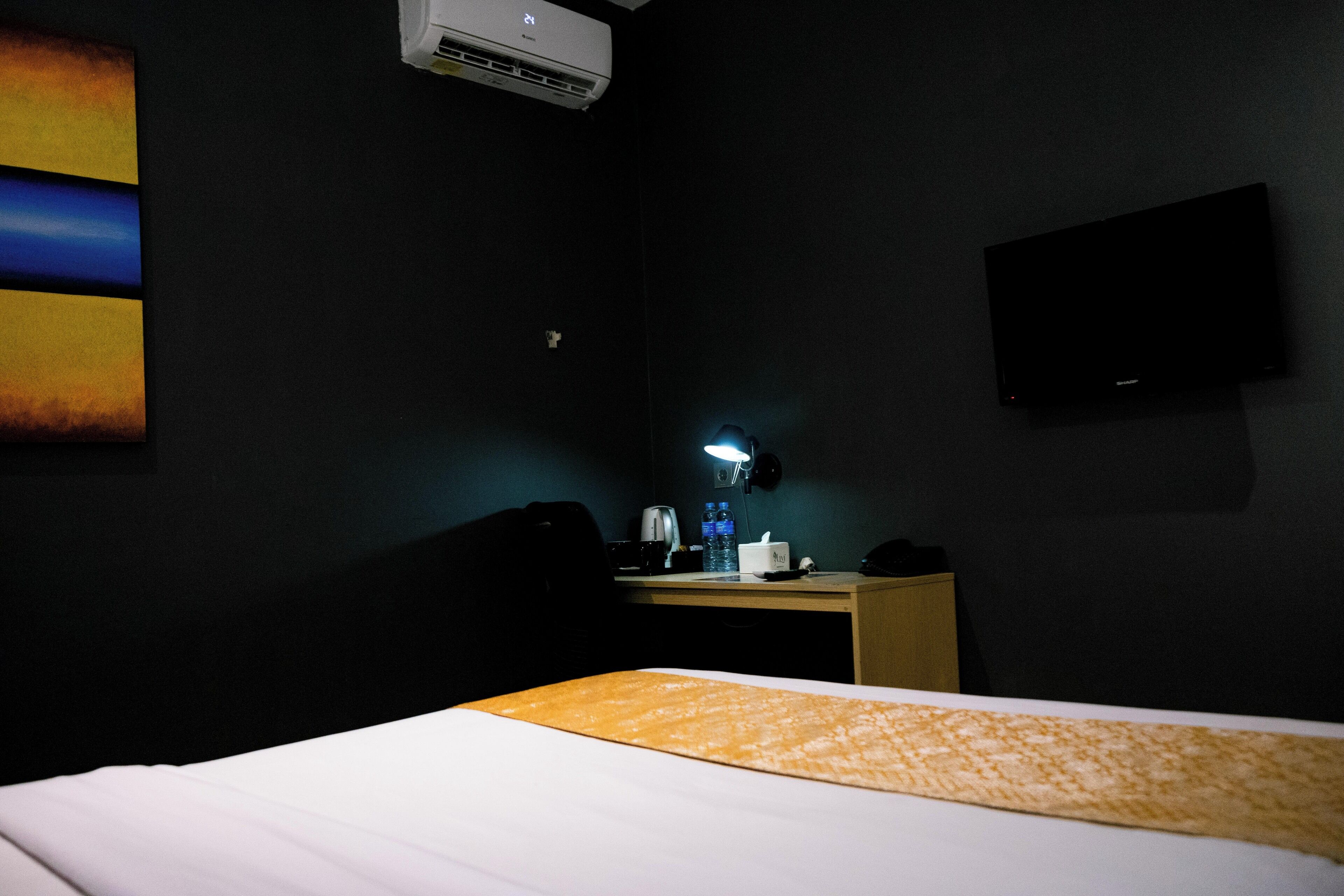 Habitación de hotel con cama, escritorio con lámpara, televisor de pantalla plana y aire acondicionado en la pared.