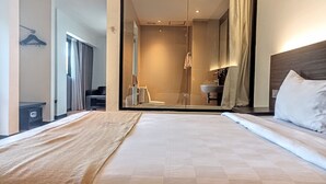 A hotel room with a large bed, a bathroom with a glass shower, and a small seating area. - Yunna Hotel (Bandar Lampung)