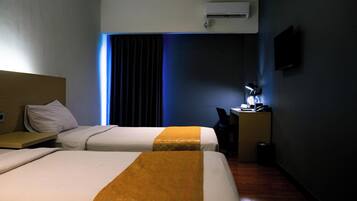 A hotel room with two beds, a desk with a chair, a TV mounted on the wall, and an air conditioning unit.
