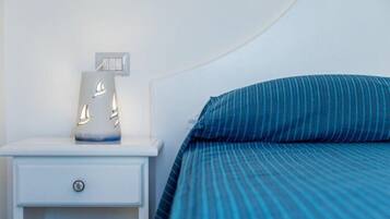 Una cama bien tendida con una colcha azul a rayas y una mesita de noche blanca con una lámpara.