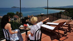 A terrace with a view of the sea, a table with a drink, and two people sitting. - Hotel Agugliastra (Baunei)