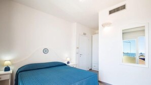 A bedroom with a bed, bedside tables, a window with a view, and a door. - Hotel Agugliastra (Baunei)