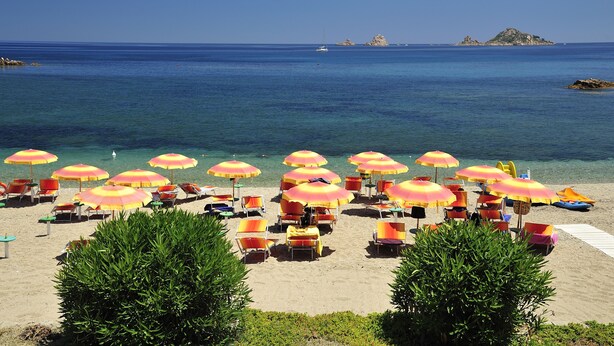 A beach with rows of sun loungers and umbrellas, clear blue water, and distant islands. - Hotel Agugliastra (Baunei)