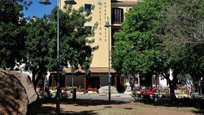 A hotel with a yellow facade, outdoor seating area, and a bell on a post. - Hotel Agugliastra (Baunei)