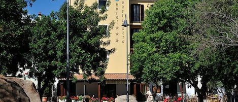 Un hotel con fachada amarilla, zona de estar al aire libre y un timbre en un poste.