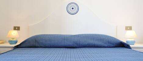 A neatly made bed with a blue-striped bedspread and a matching pillow, flanked by two bedside lamps on white nightstands.