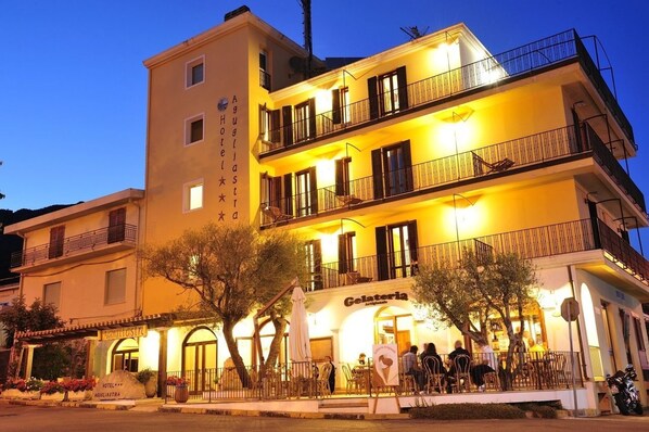 Un hotel con restaurante en la planta baja llamado "Gelateria" y un balcón con mesas al aire libre en el segundo piso.