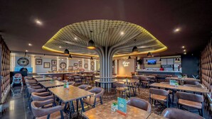 A modern restaurant interior with a central seating area, multiple tables, and a bar counter. - Griya Persada Convention Hotel & Resort Kaliurang (Pakem)