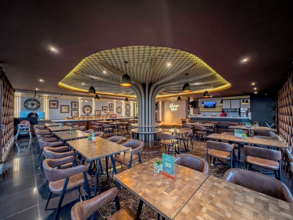 Un interior de restaurante moderno con una zona de asientos central, varias mesas y una barra.