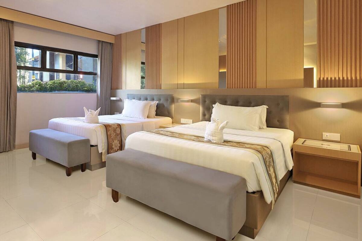 A modern hotel room with two beds, a large window, and a view of greenery outside.