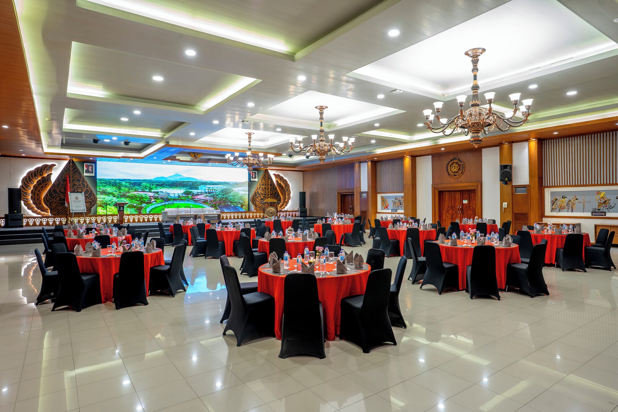 A large conference room with multiple round tables, black chairs, and red tablecloths.