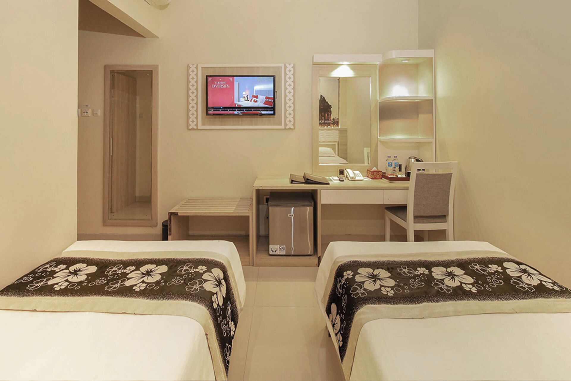 Een hotelkamer met twee bedden, een bureau met stoel, een televisie en een spiegel.