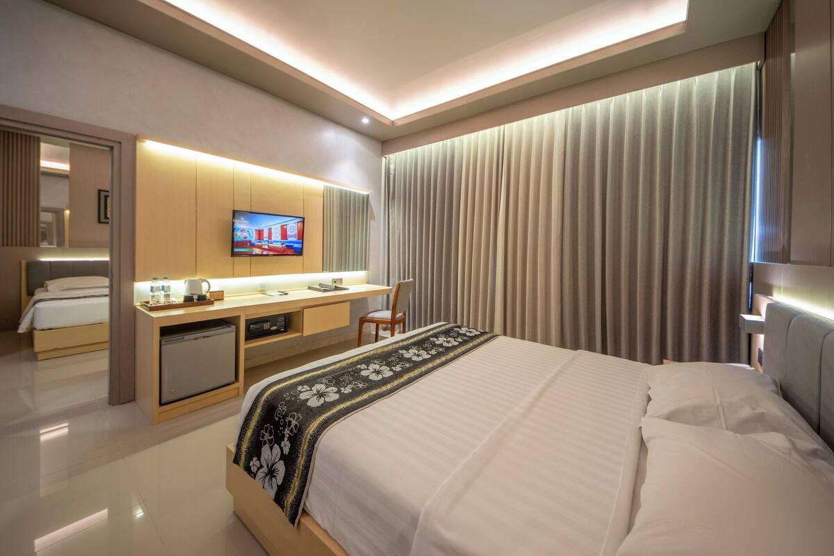 A modern hotel room with a large bed, a desk with a flat-screen TV, and a separate seating area.