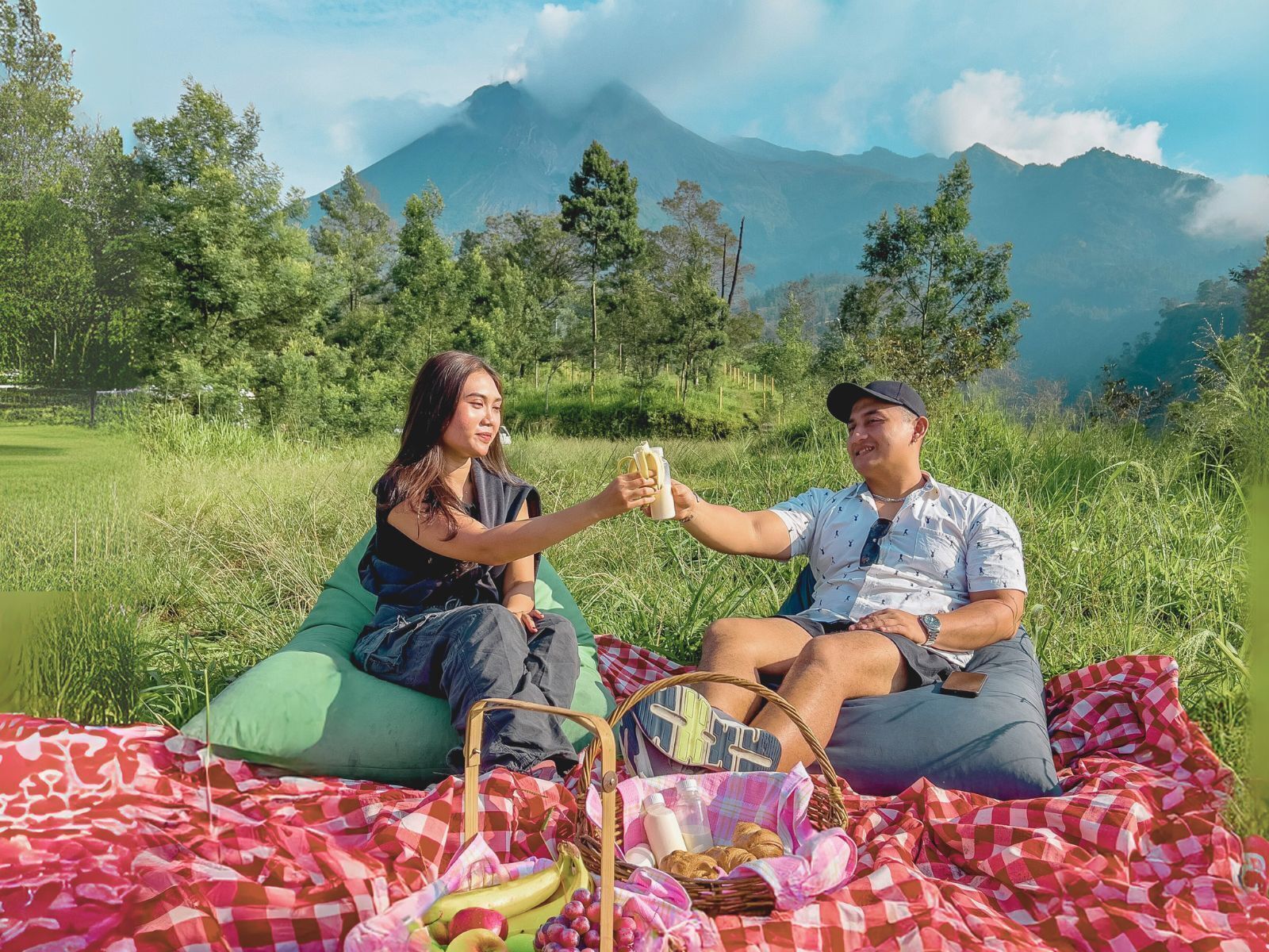 Two people sitting on bean bags in a grassy field with a mountain in the background.