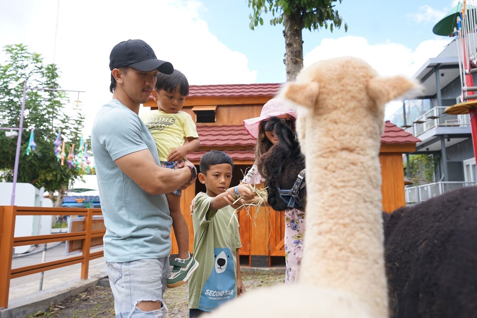 A man holding a child and another child feeding an alpaca.