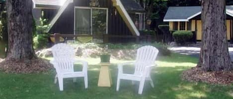 A small, triangular-shaped building with a porch, two white plastic chairs, and a table in front.