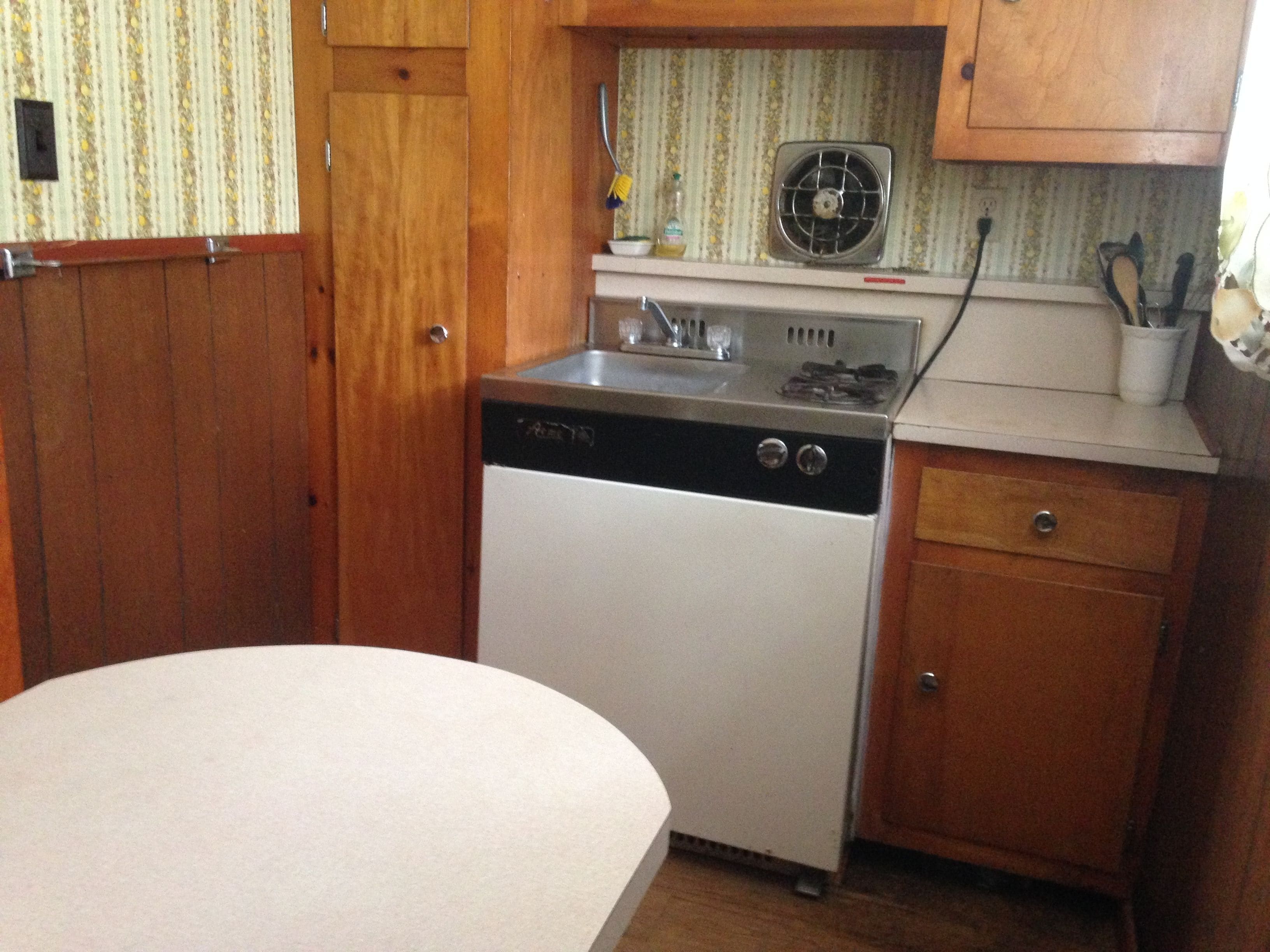 Et kompakt køkken med træskabe, opvaskemaskine, komfur og vask.