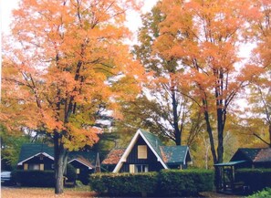 A row of cabins with a central building featuring a triangular roof, surrounded by trees with autumn foliage. - Amber Lantern Lake George Motel and Cottage Rentals (Lake George)